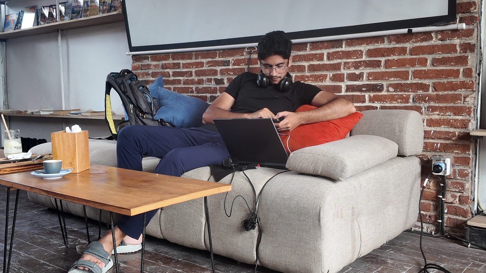 Waseem Nasir working on a laptop on a cafe couch against an exposed-brick wall