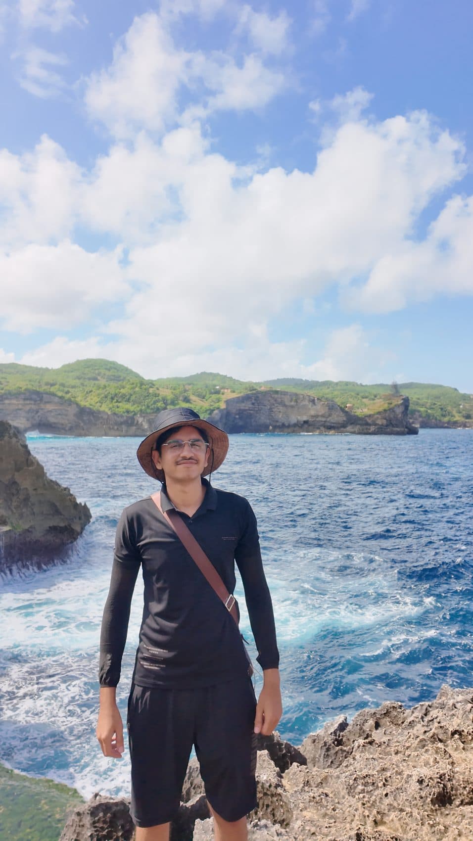 On an ocean cliff in a bucket hat with a crossbody bag